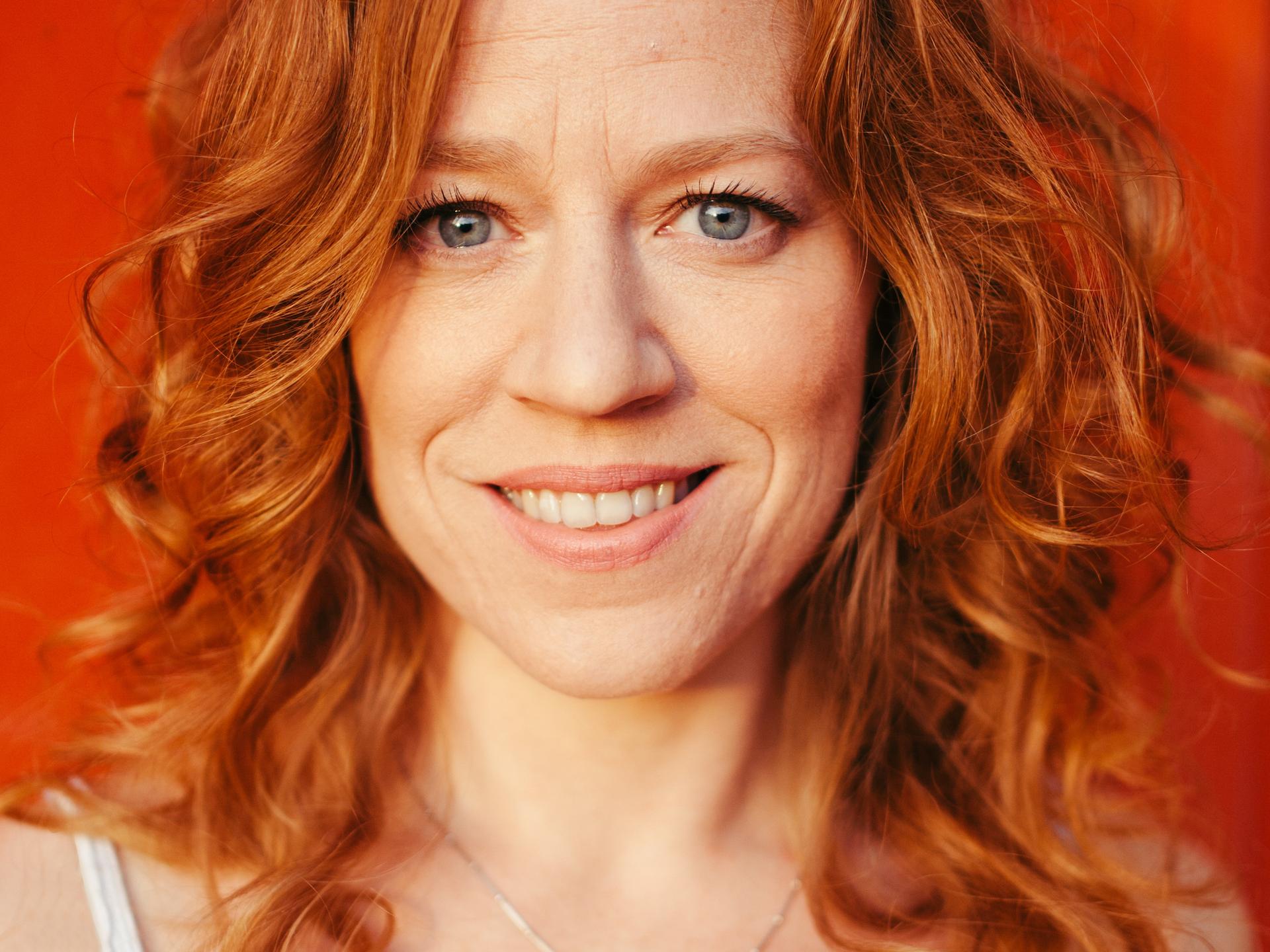 Woman with red hair smiling wearing a white vest with a necklace