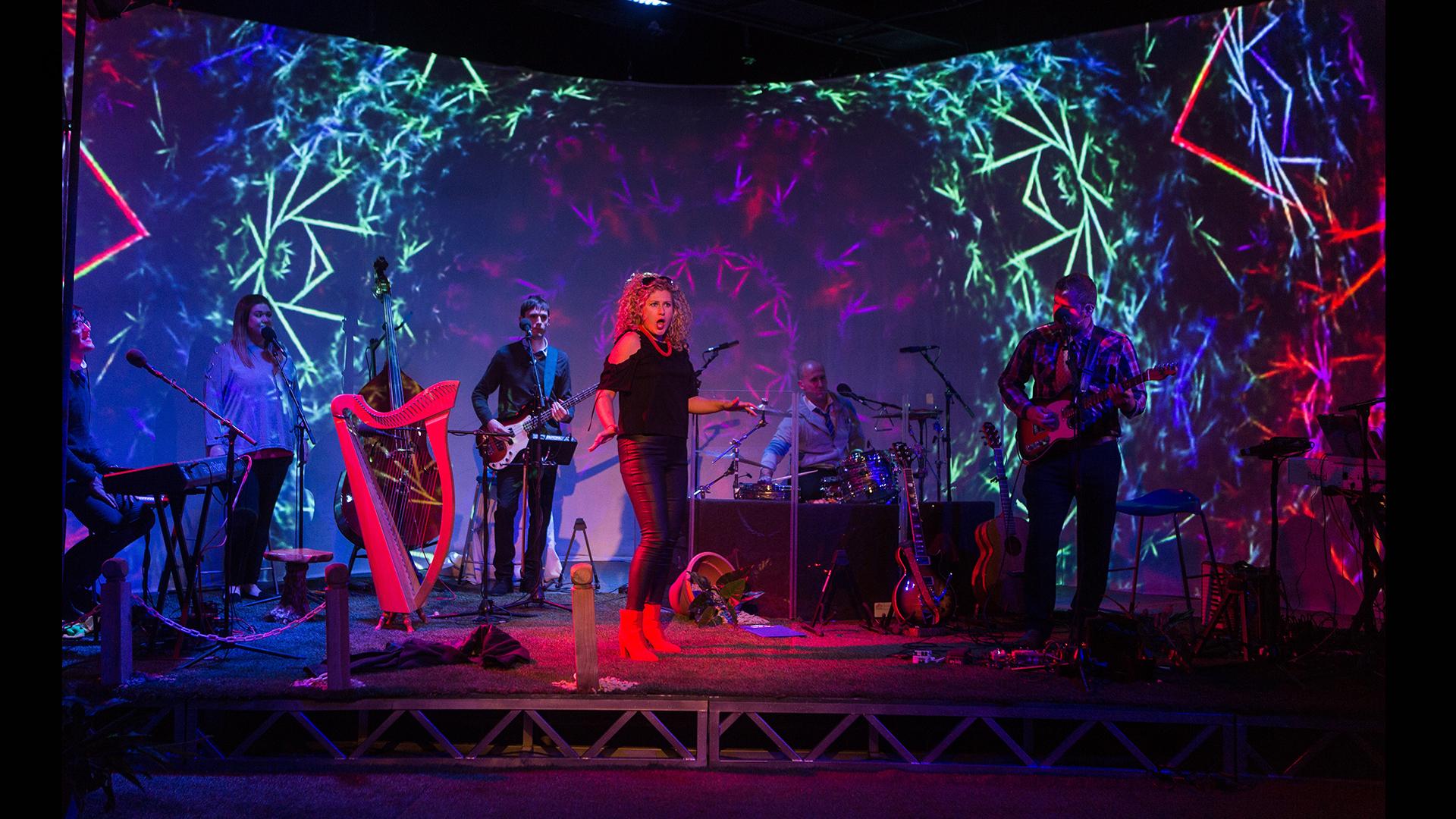 A female singer inf ront of a band with colourful patterns projected behind
