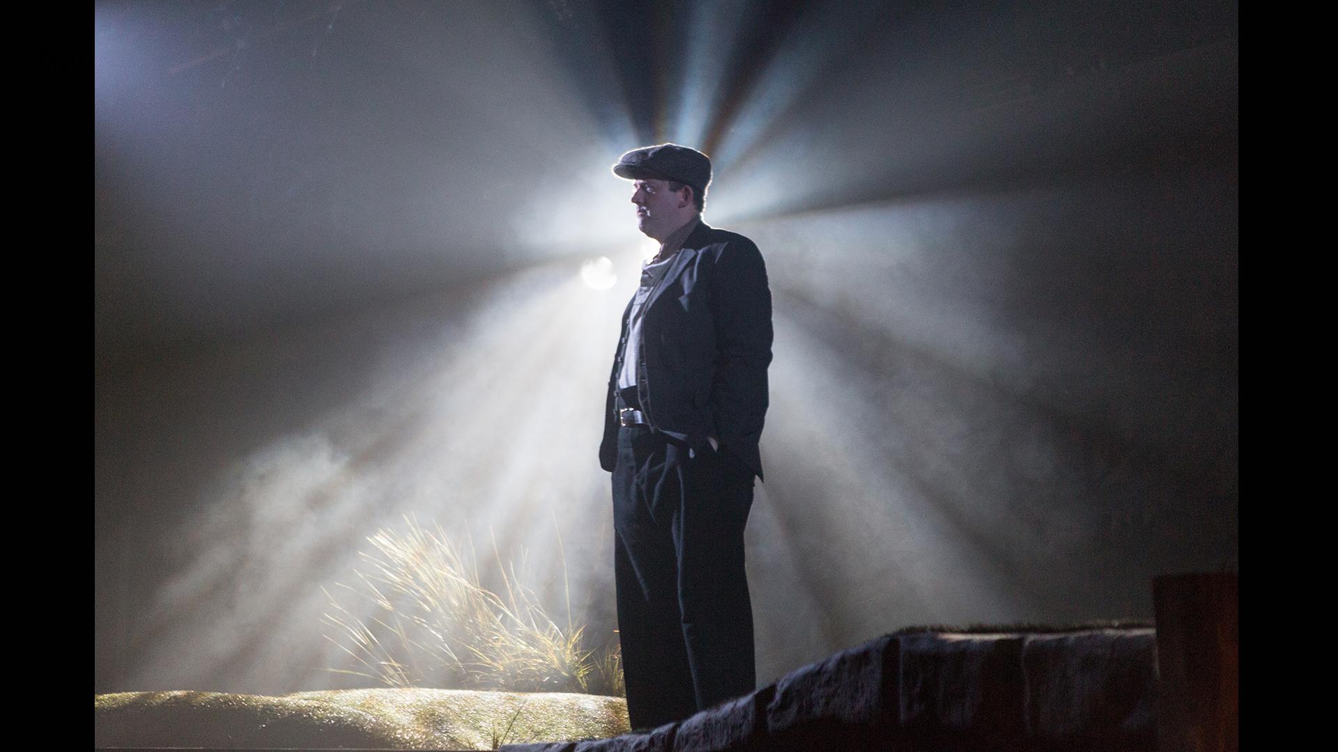 A man in a flat cap standing with light streaming behind him