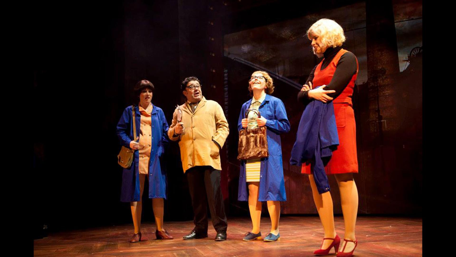 Two women and a man in work overcoats talking to a woman in a red dress