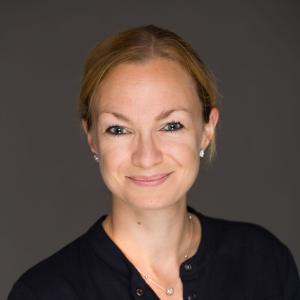 A smiling woman with dark blond hair tied back wearing a black top
