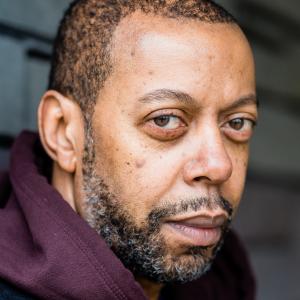 Man with black hair and facial hair wearing a burgundy hoodie