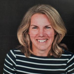Woman with dark blonde hair smiling wearing a black and white striped top