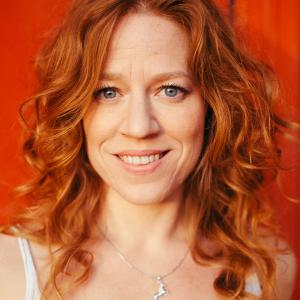 Woman with red hair smiling wearing a white vest with a necklace