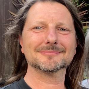 Man with long brown hair wearing a grey t-shirt